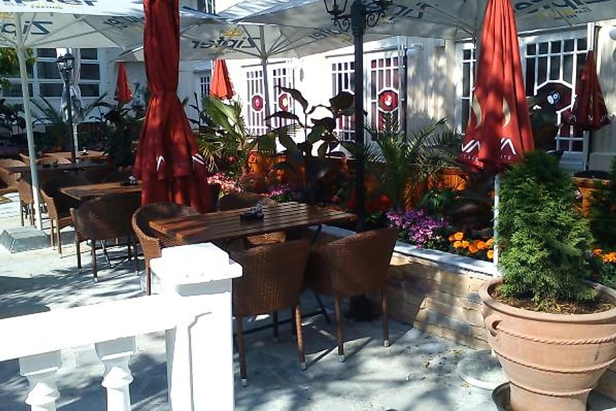 Gastgarten mit roten Sonnenschirmen, Blumenkästen und Korbstühlen im Innenhof