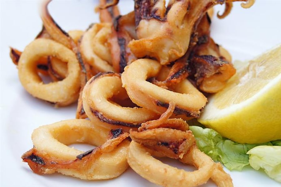 Gebackene Kalamaria-Ringe mit einer Zitronenscheibe und Salat auf weißem Teller